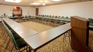 Un salón de conferencias con una mesa larga, sillas, un atril y una alfombra estampada.