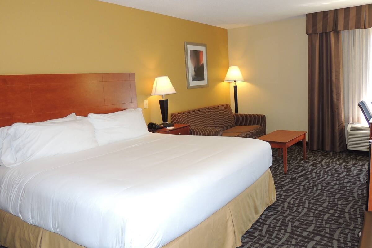 A hotel room with a large bed, a sofa, a small table, two lamps, and a window with curtains.