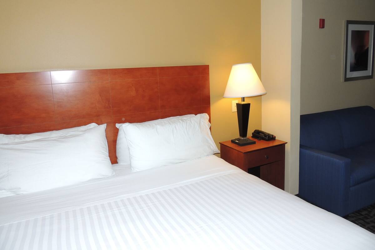 A hotel room with a large bed, a nightstand with a lamp, a phone, and a blue chair.