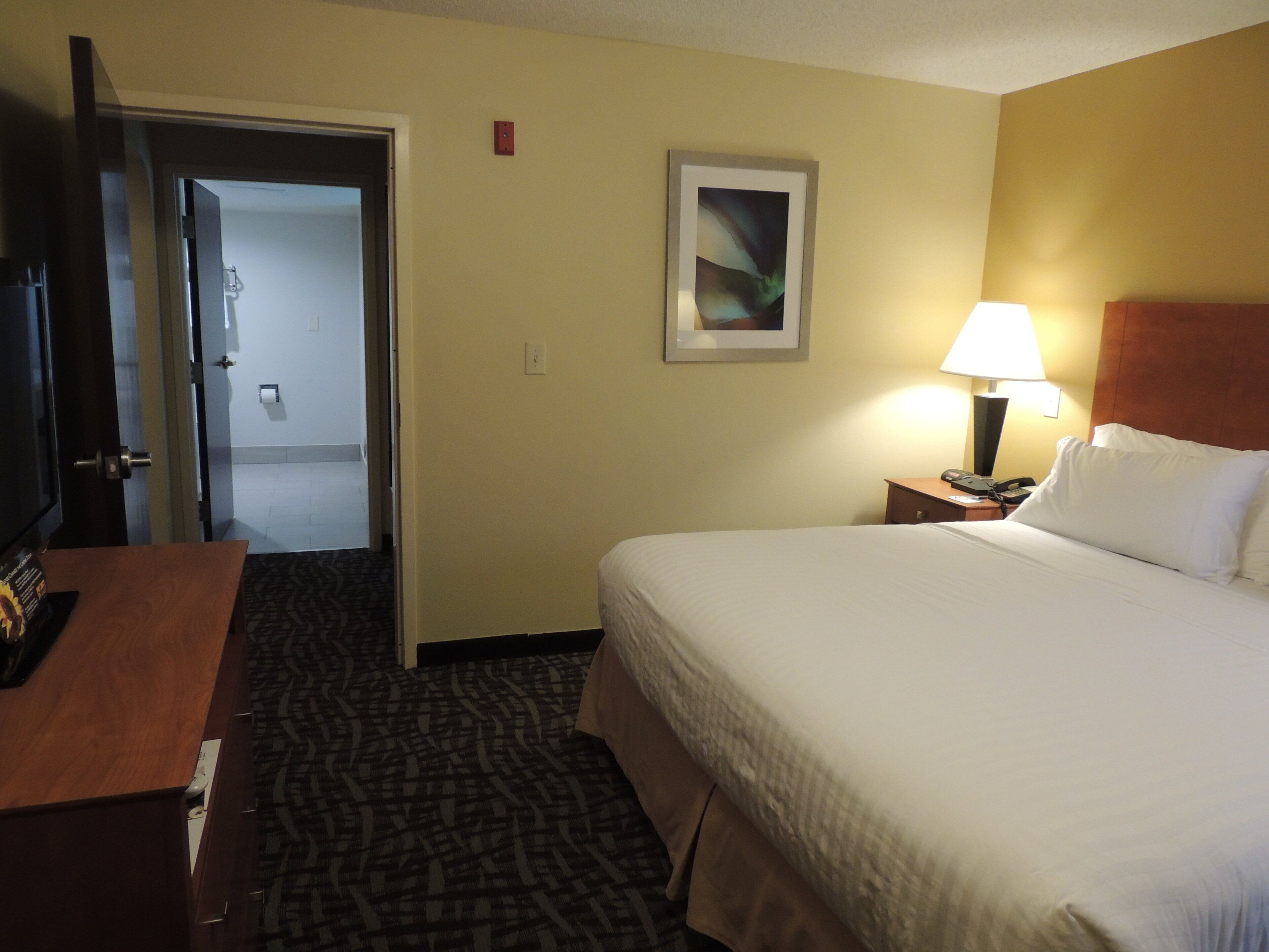 A hotel room with a bed, a desk, a lamp, and a painting on the wall.