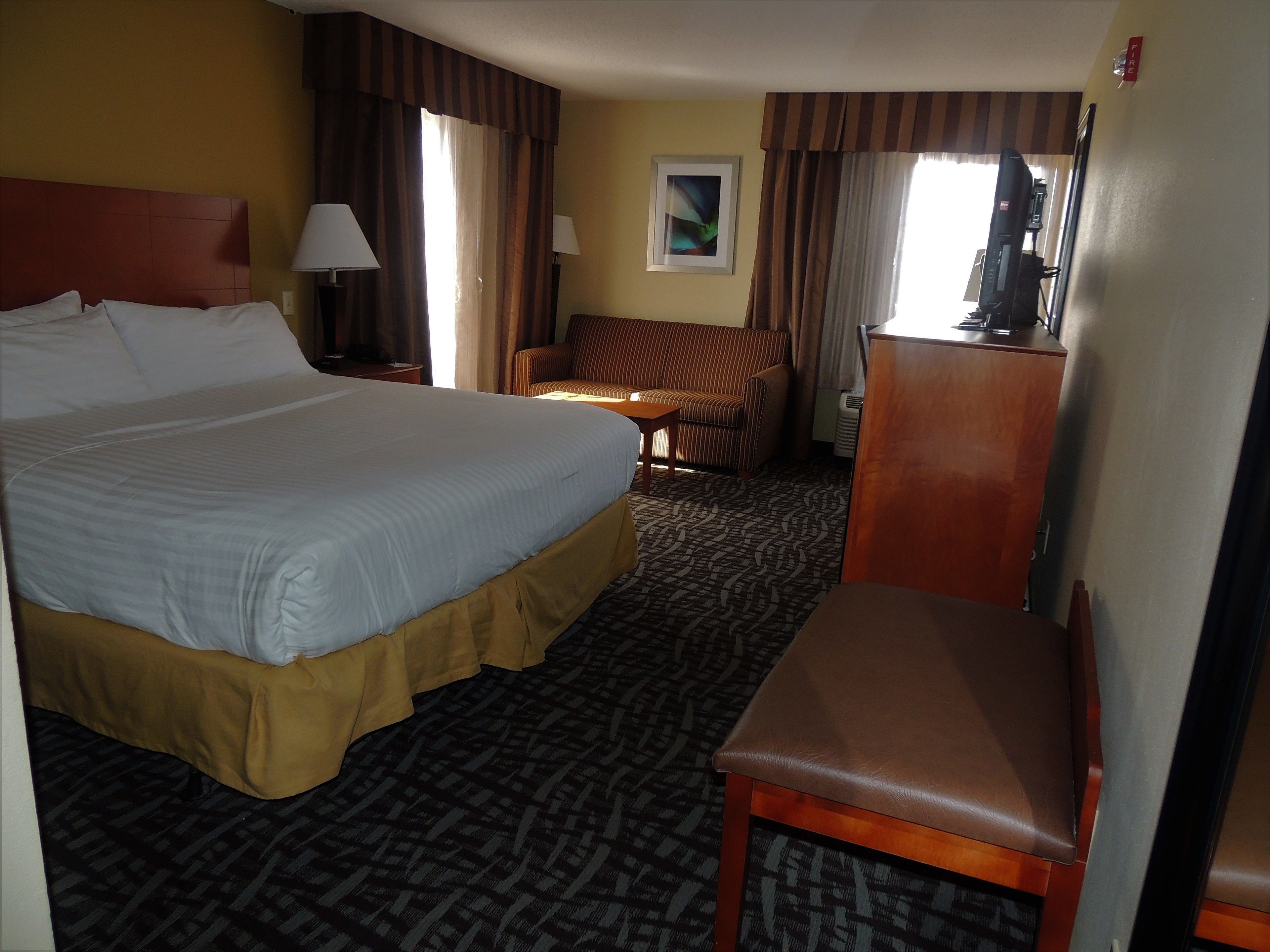 A hotel room with a large bed, a desk, a chair, and a television.