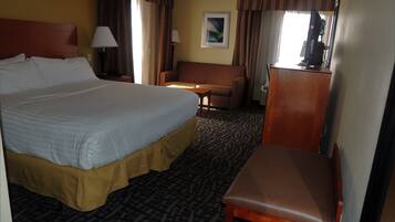 A hotel room with a large bed, a desk, a chair, and a television.
