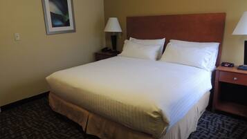 A hotel room with a large bed, two bedside tables, a nightstand, a framed picture on the wall, and a patterned carpet.