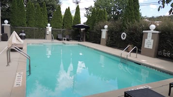 A rectangular pool with a clear blue water surface, surrounded by a low concrete deck. There are metal handrails on the pool's edge, and a lifebuoy attached to the wall. The pool area is enclosed by a metal fence with decorative posts topped with spherical objects.