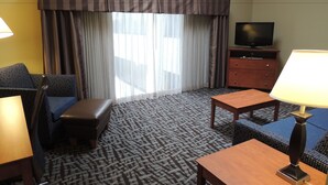 Habitación de hotel con sofá, una mesita, televisor en una cómoda y alfombra estampada.