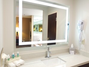 A hotel bathroom with a large mirror, a sink, a hairdryer, and toiletries on the counter.