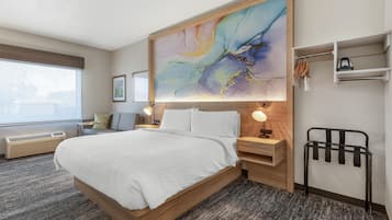 A hotel room with a large bed, bedside tables, a wall-mounted heater, a radiator, a towel rack, and a large abstract painting.