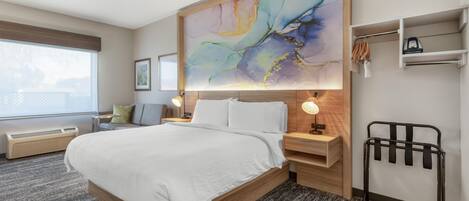 Habitación de hotel con una cama grande, mesitas de noche, un calentador fijado a la pared, un radiador, un perchero para toallas y un cuadro abstracto de gran tamaño.