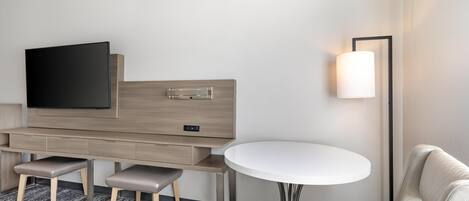 Una habitación de hotel moderna con una televisión de pantalla plana, un escritorio de madera con cajones, una mesa redonda y un sofá.