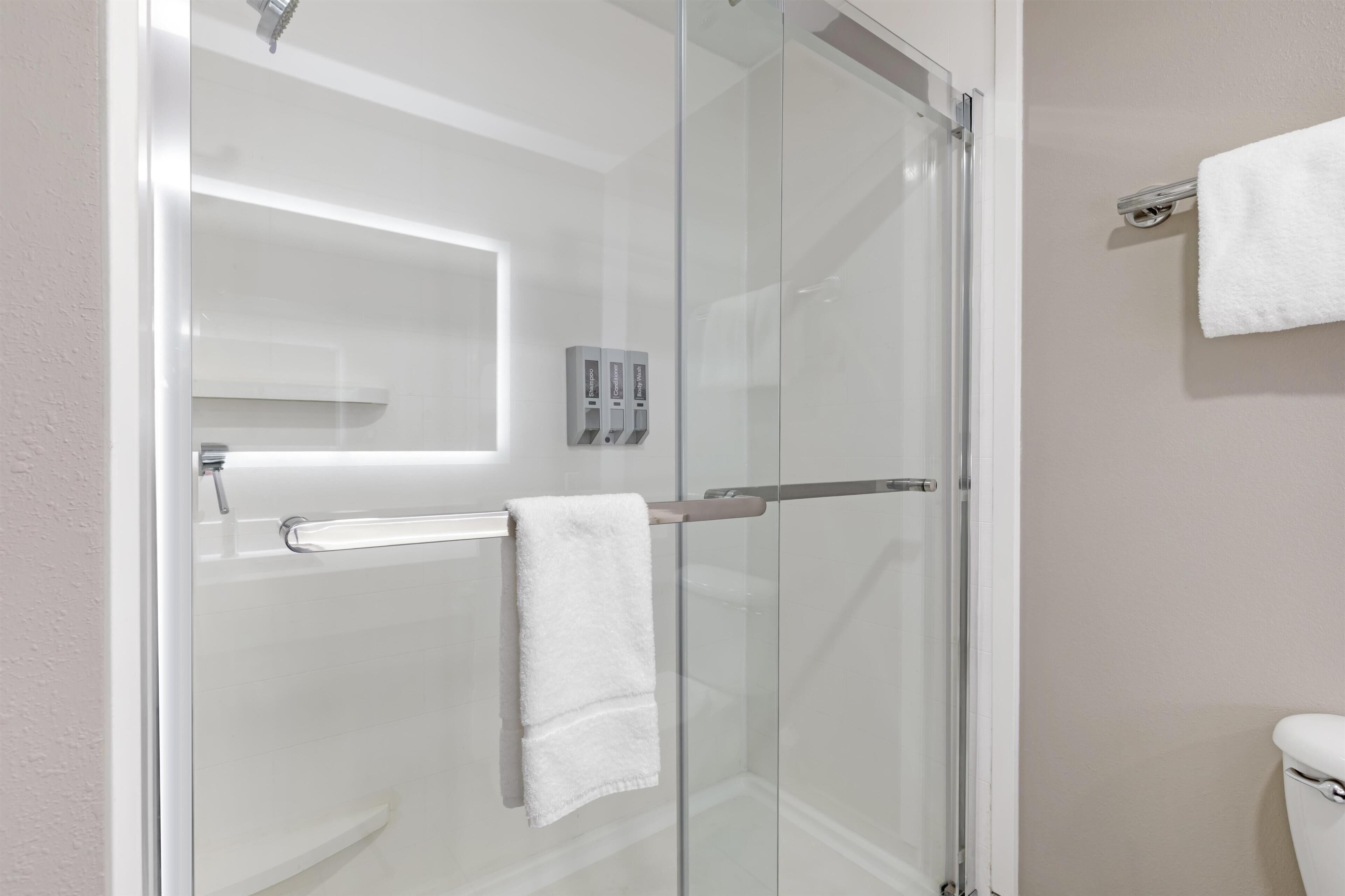 Une douche fermée par des parois en verre, dotée d’un porte-serviettes, de toilettes et d’un distributeur de serviettes fixé au mur.
