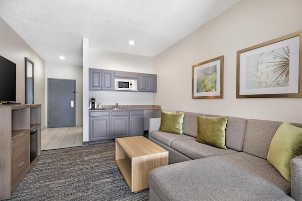A modern living room with a grey sofa, a wooden coffee table, and a kitchen in the background.