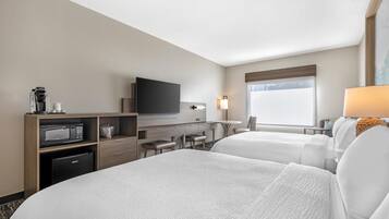 Habitación de hotel con dos camas, un escritorio, televisor, microondas y refrigerador pequeño.