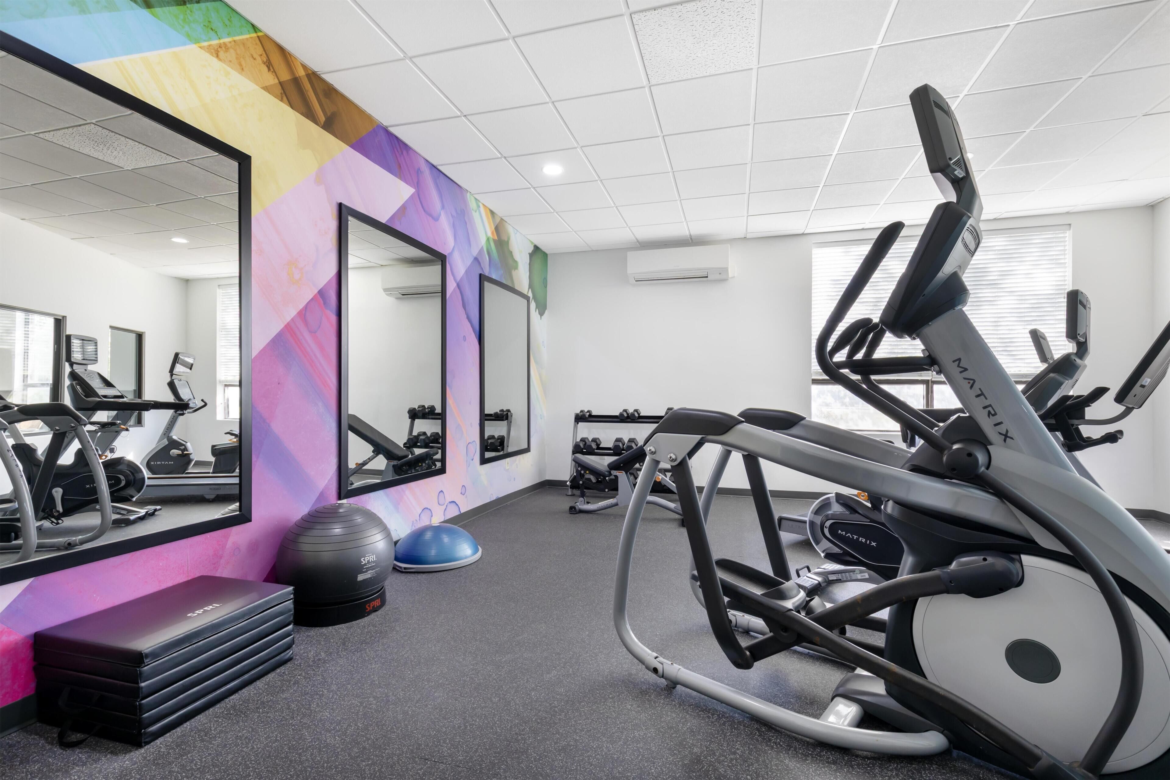 A gym with exercise equipment, a mirrored wall, and a colorful geometric design on the wall.