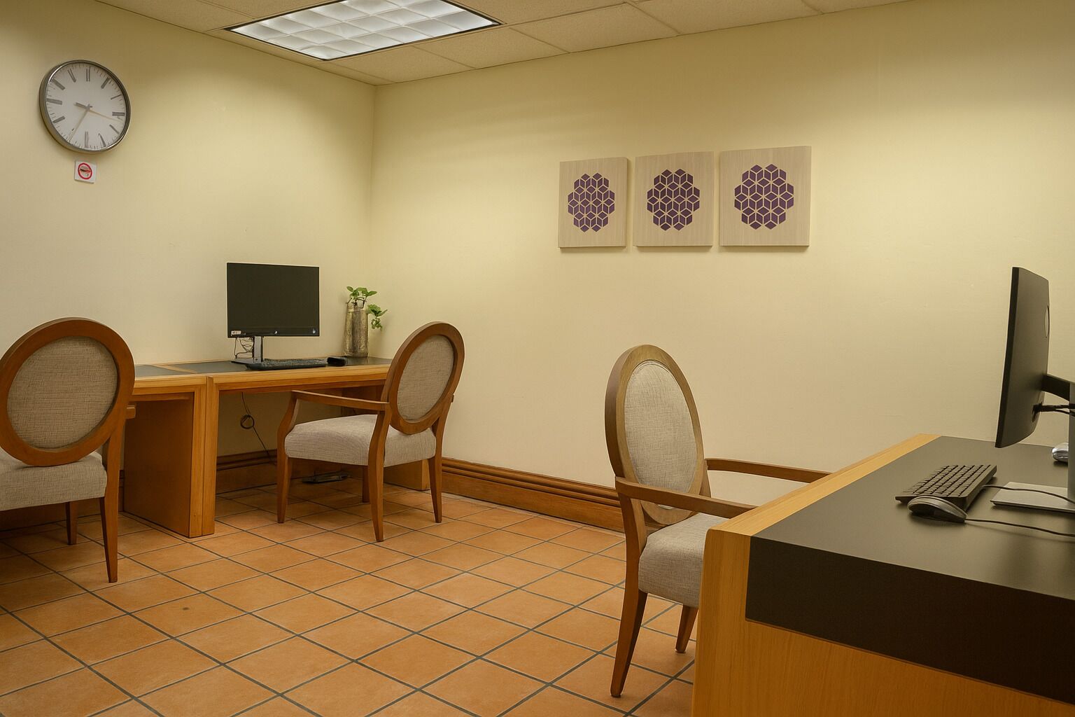 A room with a desk, two chairs, a computer monitor, a keyboard, and a clock on the wall.