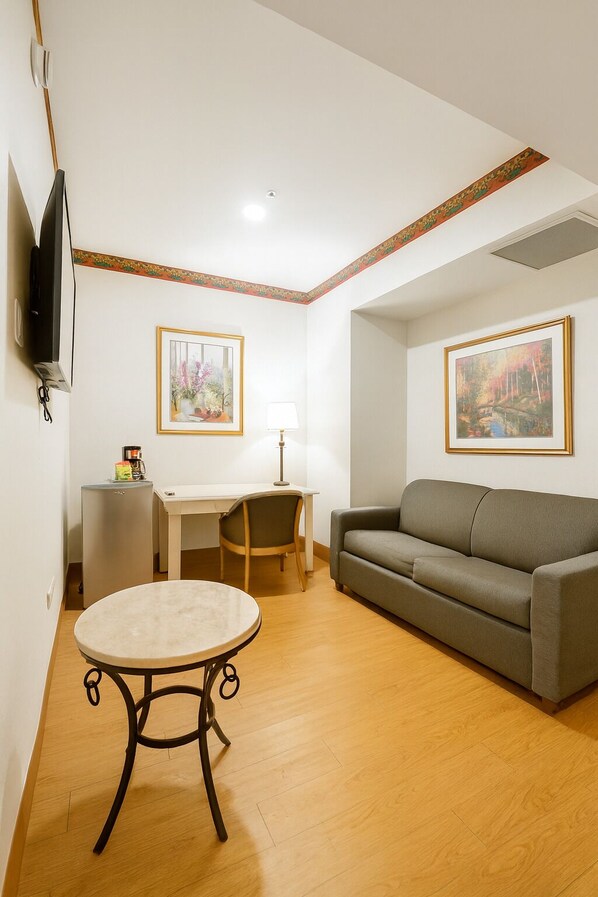 A living room with a sofa, a small table, a desk, and two framed pictures on the walls. - iStay Hotel Ciudad Victoria (Ciudad Victoria)
