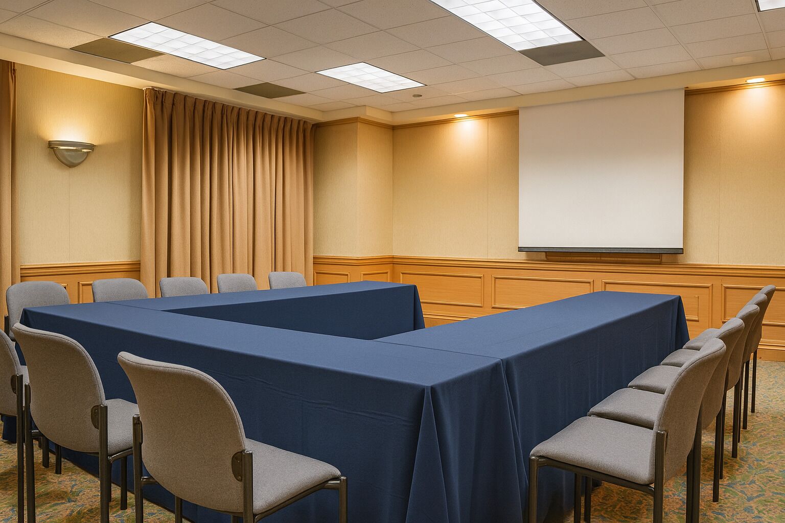 Una sala de conferencias con una mesa larga, sillas, una pantalla de proyector y una cortina.