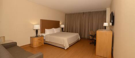 A hotel room with a bed, a desk, a chair, a sofa, and a TV on the wall.