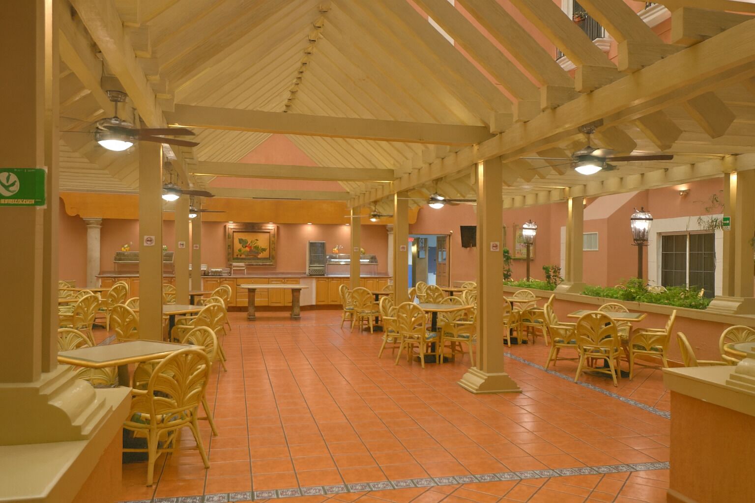A spacious indoor dining area with numerous tables and chairs, a tiled floor, and a high ceiling with wooden beams.