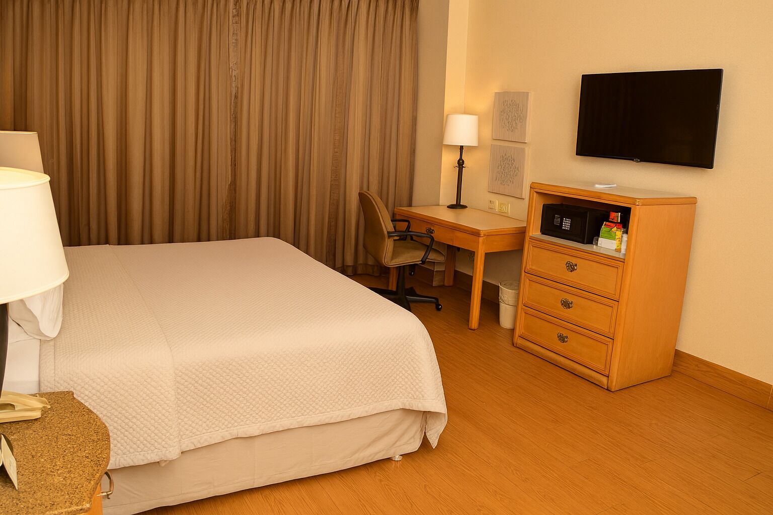 A hotel room with a bed, desk, chair, TV, and a minibar.