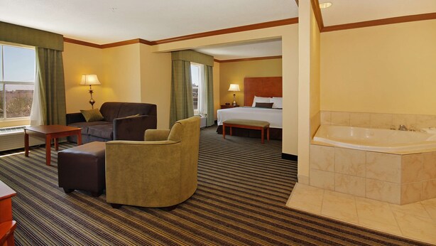 Une chambre d’hôtel dotée d’un grand lit, d’un coin salon avec un canapé et un fauteuil, d’une petite table, d’un banc et d’une salle de bain séparée avec une baignoire.