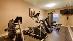 Une salle de sport à domicile équipée de divers appareils d’exercice, notamment un tapis de course, un vélo elliptique et des appareils de musculation.