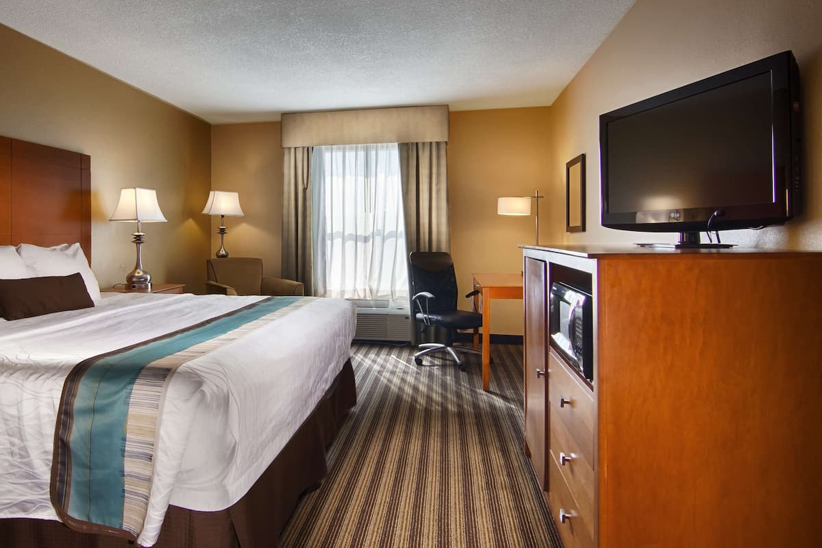 Een hotelkamer met een groot bed, twee bedlampjes, een flatscreen televisie, een bureau met stoel en een magnetron.