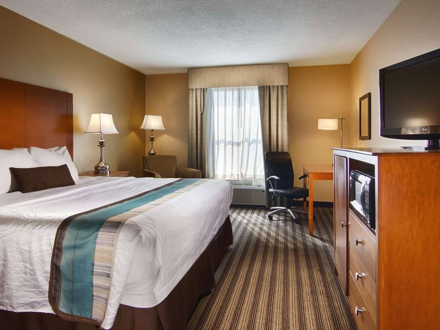 A hotel room with a large bed, two bedside lamps, a flat-screen TV, a desk with a chair, and a microwave.