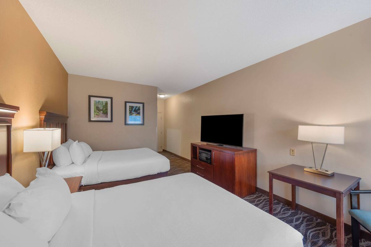 A hotel room with two beds, a TV, a desk, and a lamp.