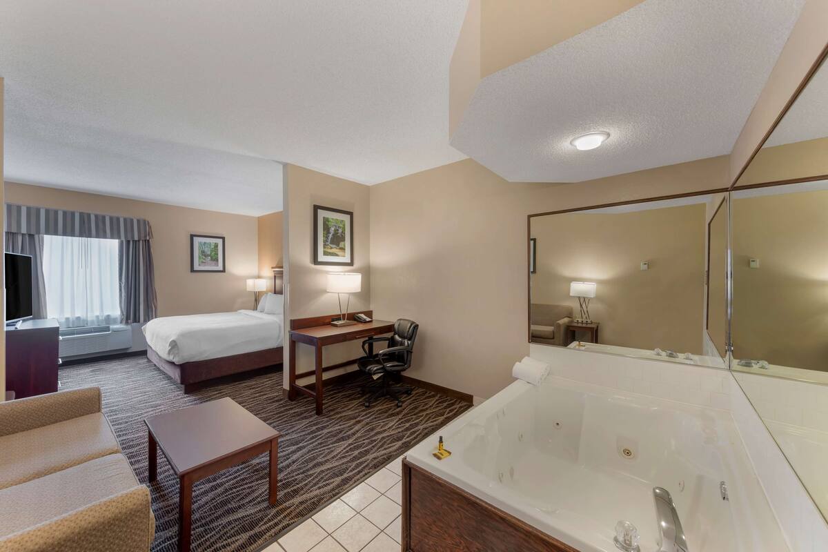 A hotel room with a bed, desk, chair, and a large bathtub.