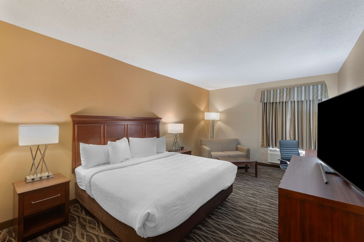 A hotel room with a large bed, two bedside tables with lamps, a desk with a TV, a chair, and a window with curtains.