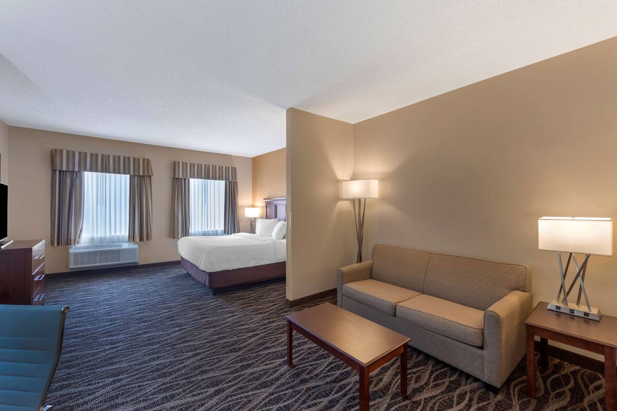 A hotel room with a bed, a sofa, a coffee table, a TV, and a lamp.