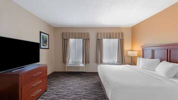 A hotel room with a bed, a TV on a wooden dresser, and two windows with curtains.