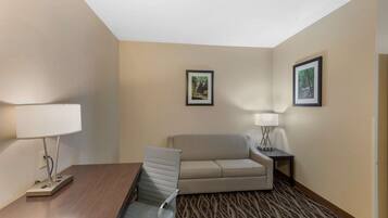 A hotel room with a desk, two chairs, a sofa, two lamps, and two framed pictures on the wall.