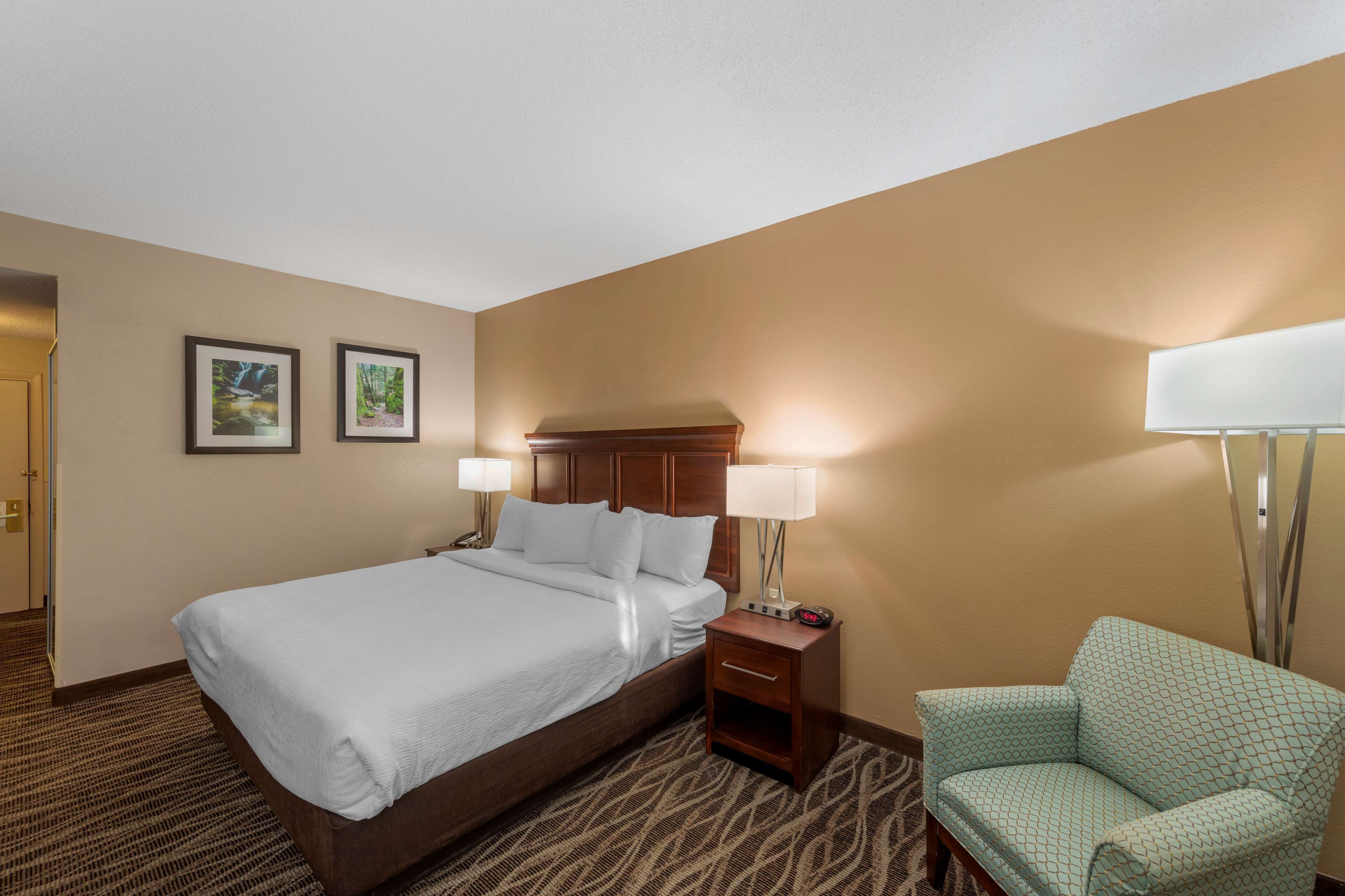 A hotel room with a large bed, two bedside lamps, a nightstand, a chair, and two framed pictures on the wall.