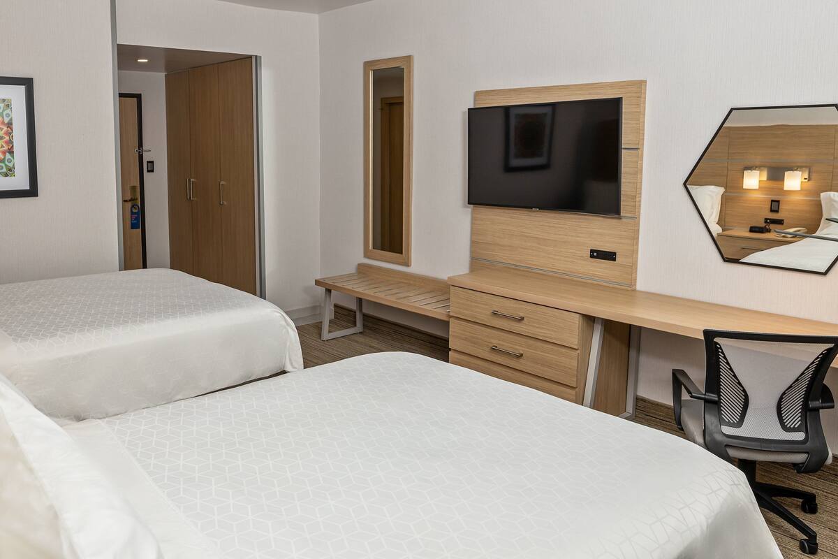 A hotel room with two beds, a desk with a chair, a TV, and a mirror.