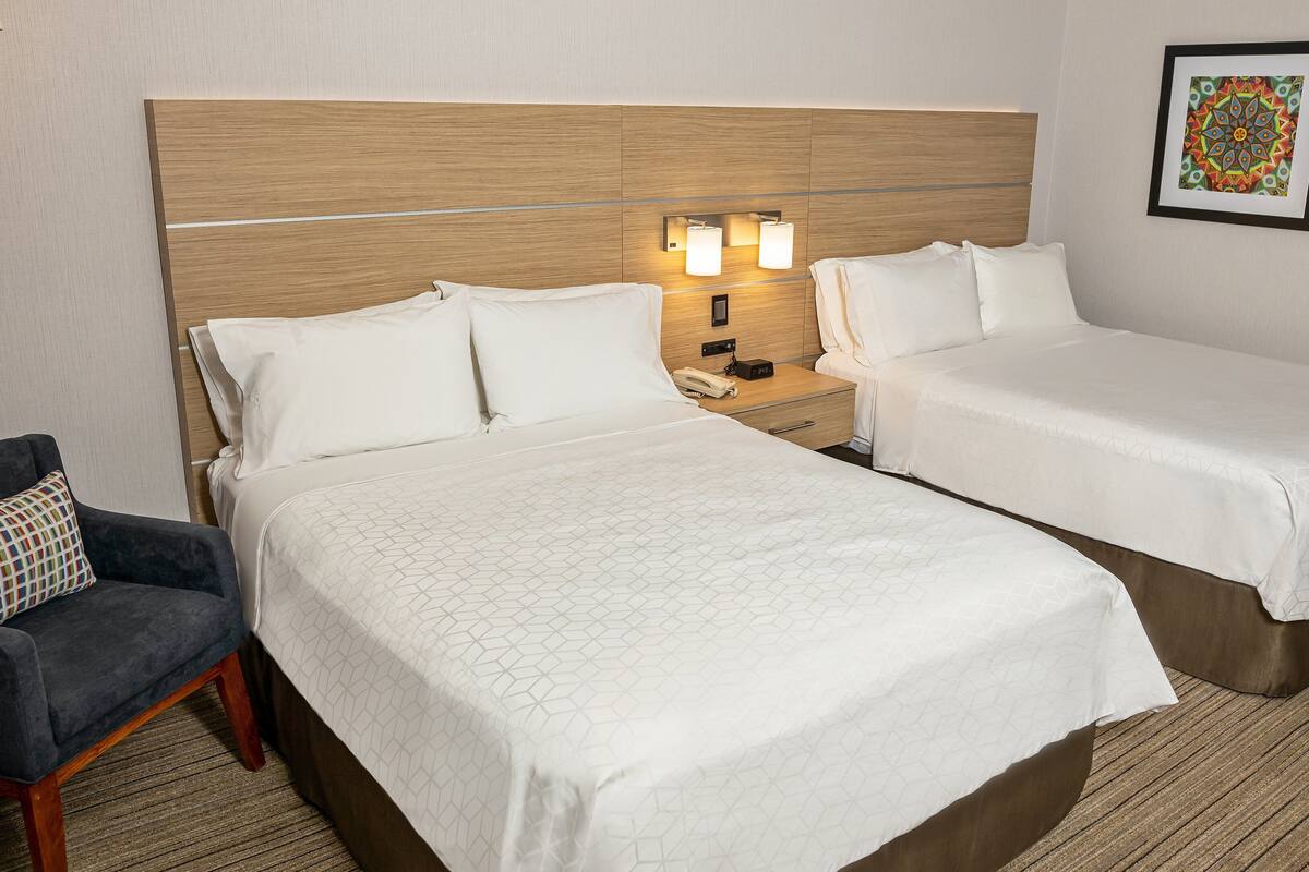 A hotel room with two beds, a nightstand with a phone and lamp, a chair, and a wall-mounted picture.