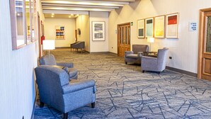 A hotel lobby with a patterned carpet, seating area with armchairs, a piano, and framed artwork on the walls. - Holiday Inn Express Chihuahua by IHG (Chihuahua)