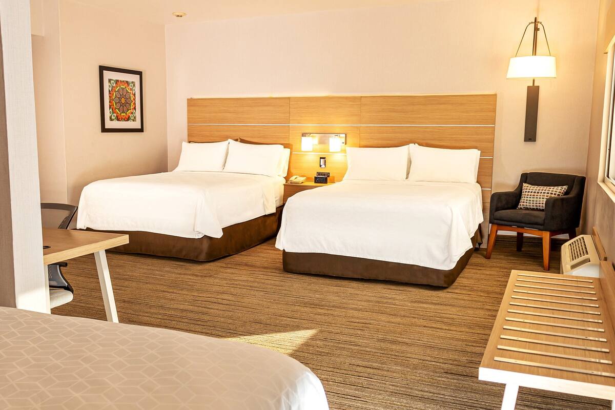 A hotel room with two beds, a wooden headboard, bedside lamps, a chair, and a small table.