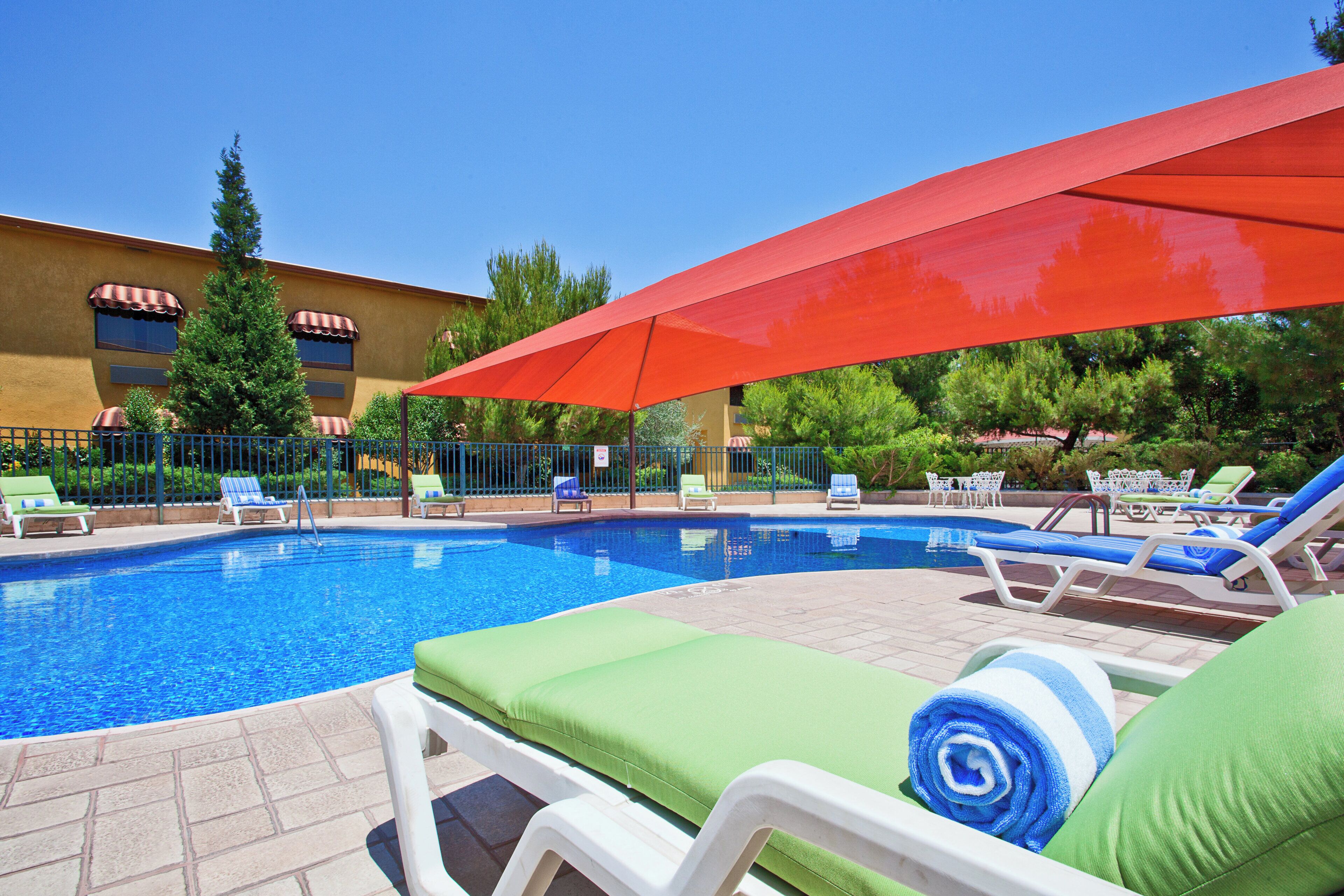 Zona de piscina con sillones de descanso y una sombrilla roja.
