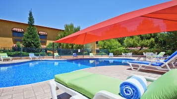 Zona de piscina con sillones de descanso y una sombrilla roja.
