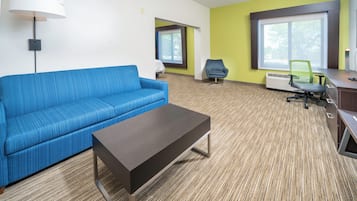 A modern hotel room with a blue sofa, a dark wooden coffee table, and a green chair.