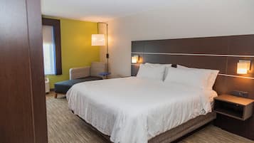 Habitación de hotel con una cama grande, mesitas de noche, una lámpara de pared y una pequeña zona de estar con una silla y una mesa.