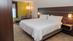 A hotel room with a large bed, bedside tables, a small seating area, and a wall-mounted lamp. - Holiday Inn Express Clayton (Se Raleigh) by IHG (Garner)