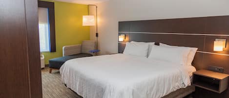 A hotel room with a large bed, bedside tables, a small seating area, and a wall-mounted lamp.