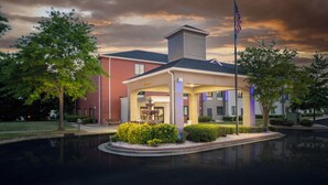 A hotel with a covered outdoor area, a flagpole, and a reflective pool. - Holiday Inn Express Clayton (Se Raleigh) by IHG (Garner)