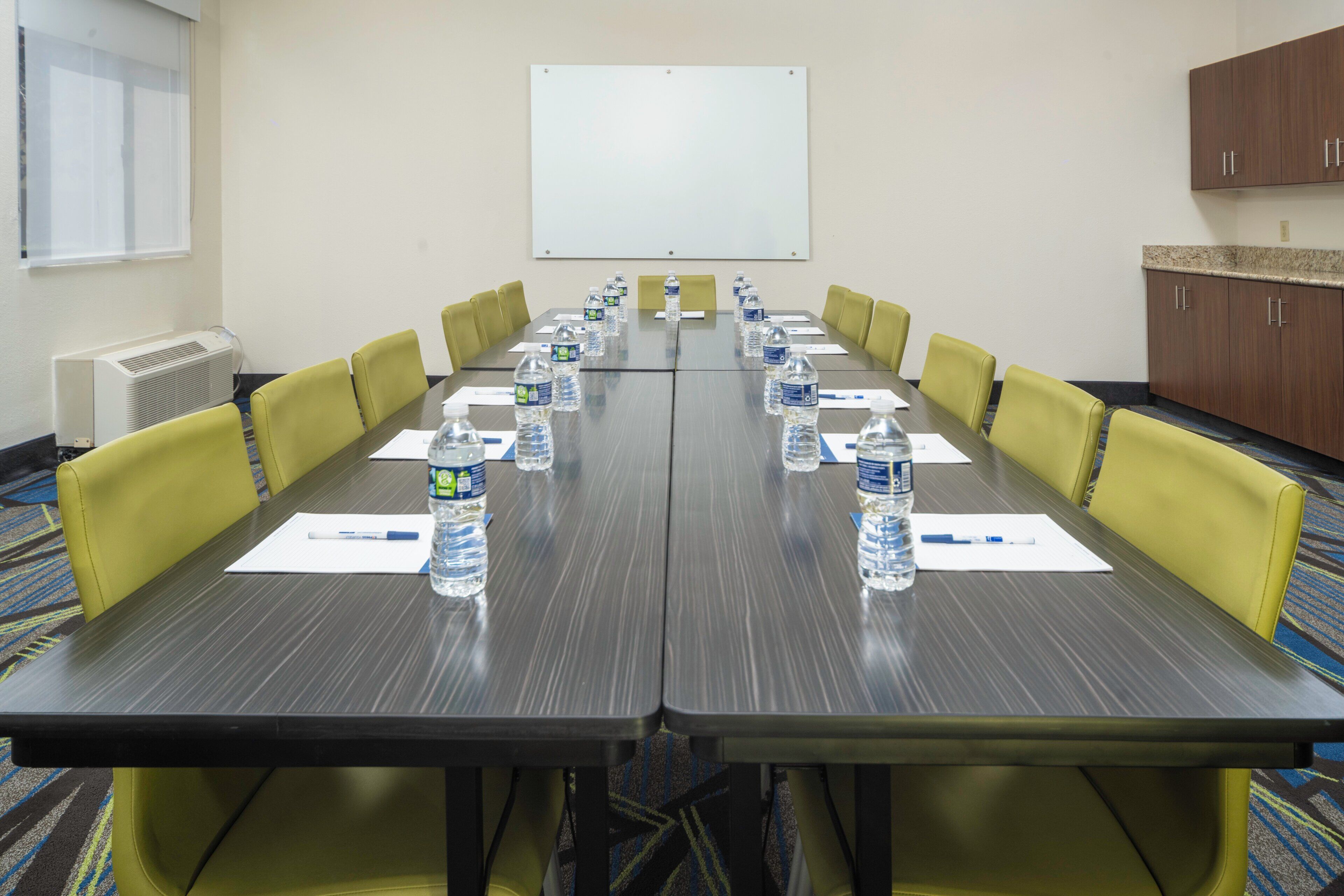 A conference room with a long table, yellow chairs, water bottles, and a whiteboard on the wall.