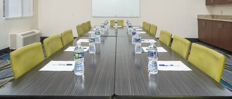 A conference room with a long table, yellow chairs, water bottles, and a whiteboard on the wall.