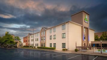 A multi-story hotel with a flat roof, large windows, and a parking lot in front.