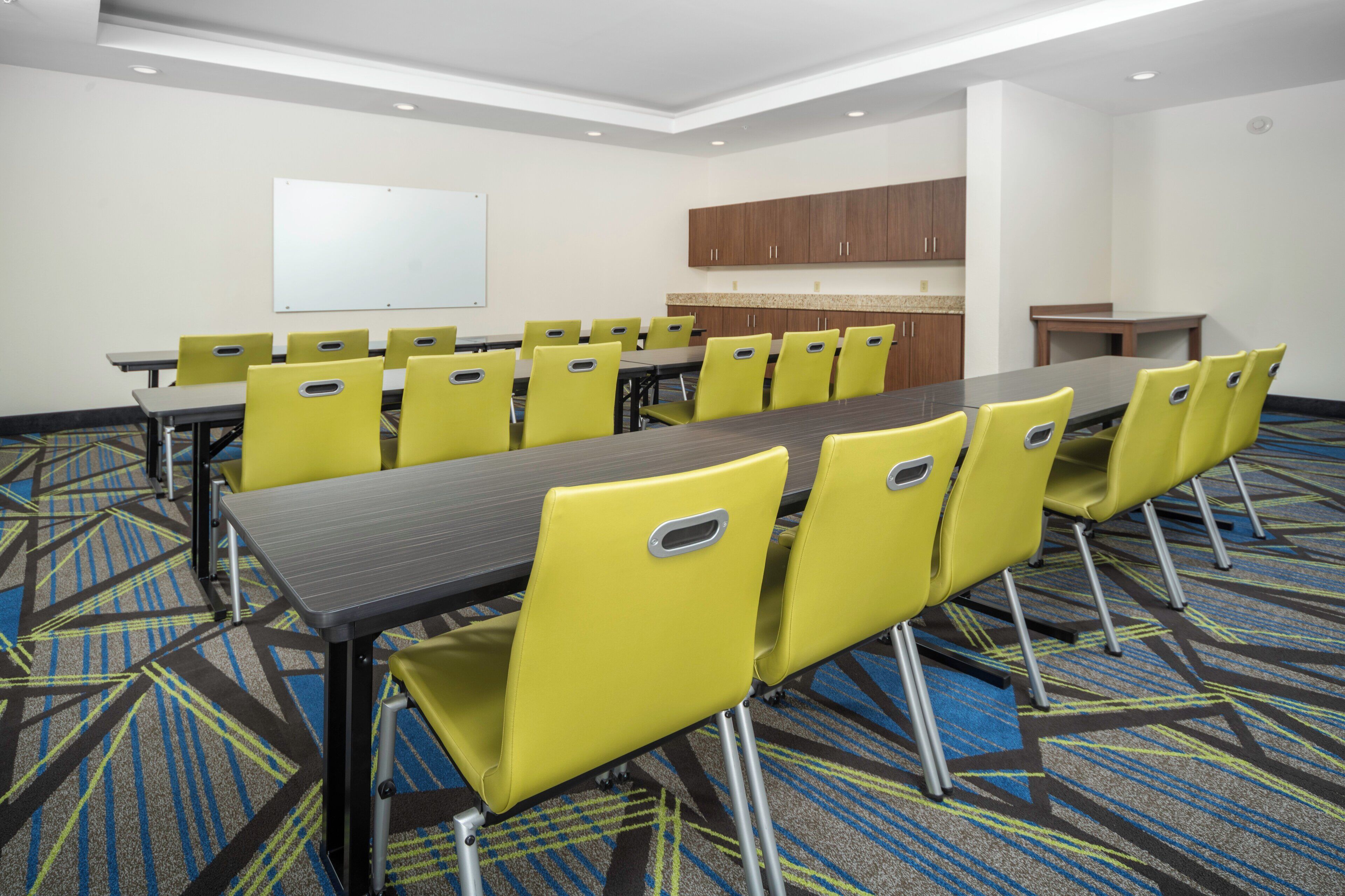 Une salle de conférence avec une longue table et des chaises jaunes, un tableau blanc et, au fond, un coin cuisine.