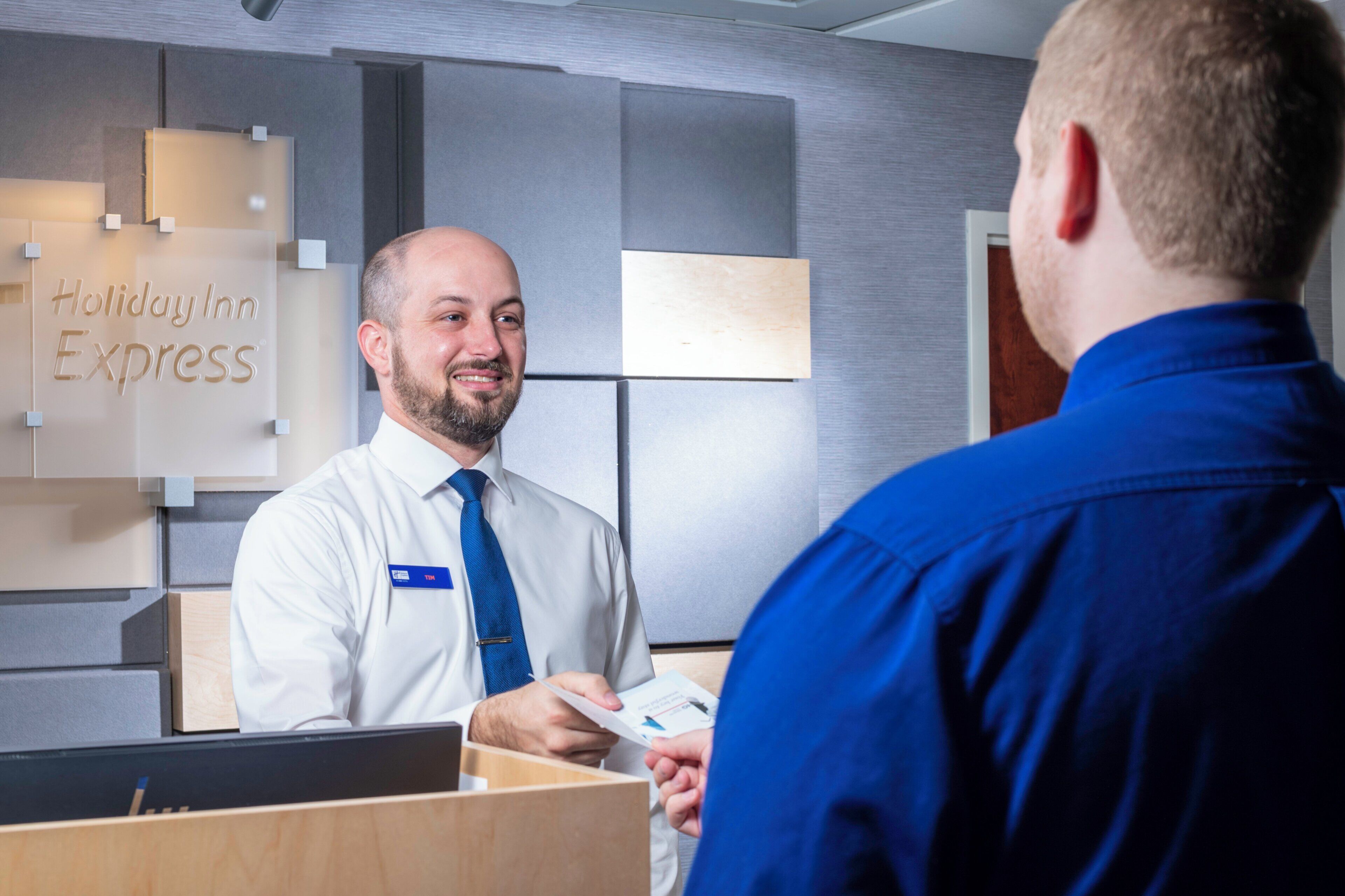 A hotel reception desk with a sign reading 'Holiday Inn Express' and a man in a blue shirt interacting with a staff member.